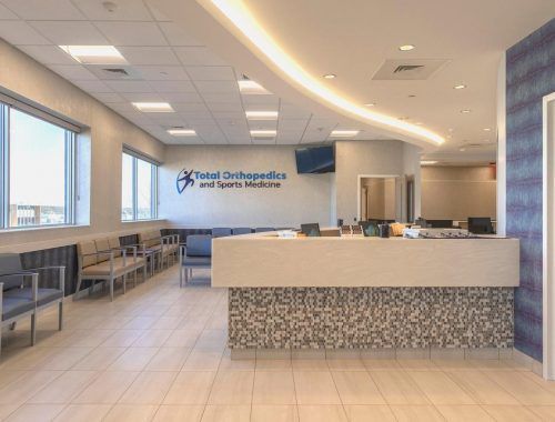 Bright orthopedic clinic reception area with waiting chairs, front desk, and large windows