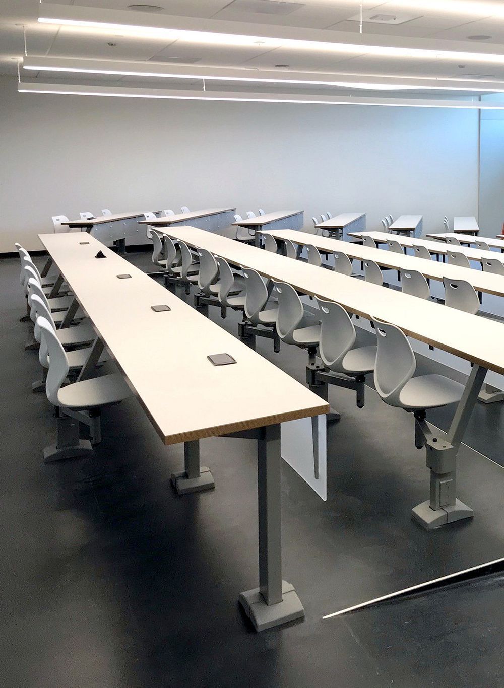 Empty modern classroom with long white tables, gray chairs, and overhead fluorescent lights