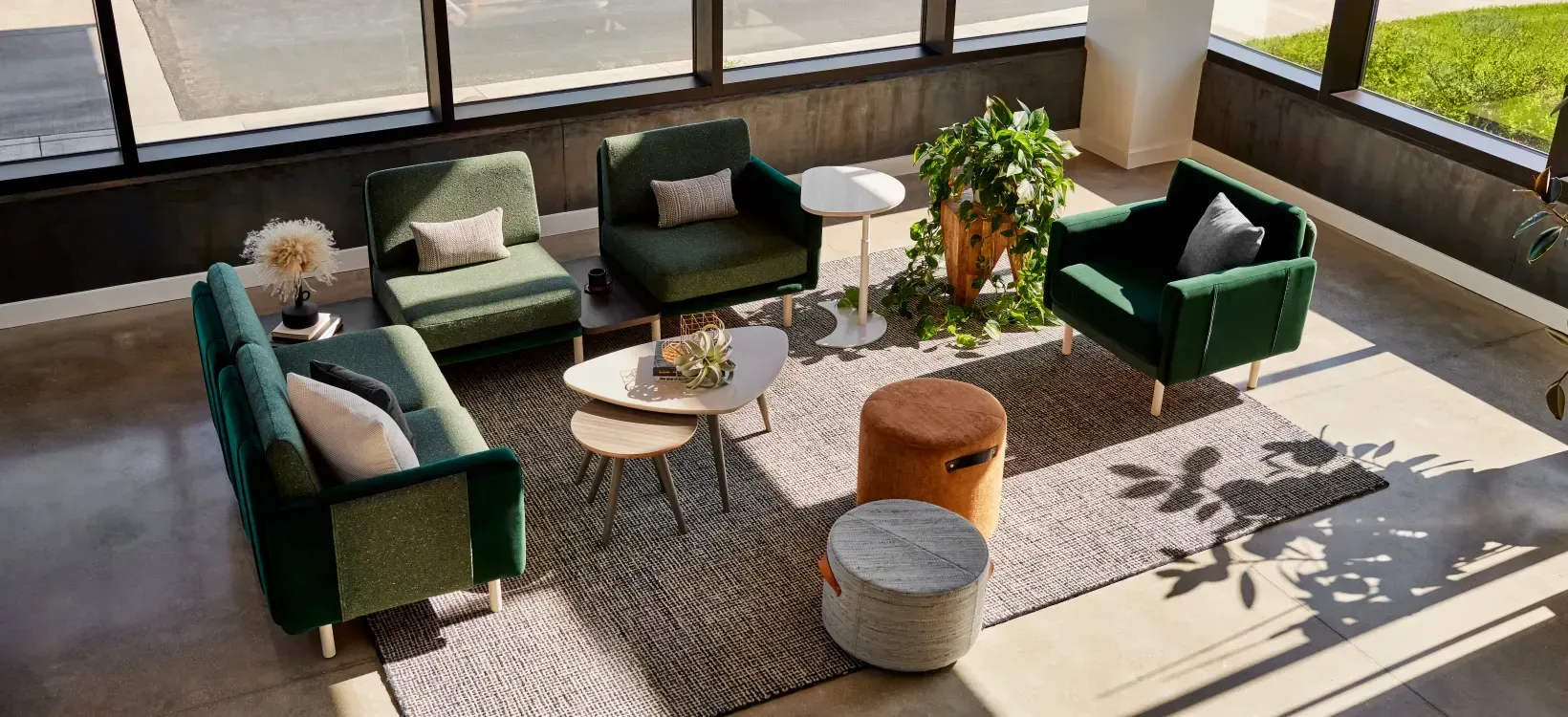 Sunny lounge with green sofas, round tables, and plants by large windows
