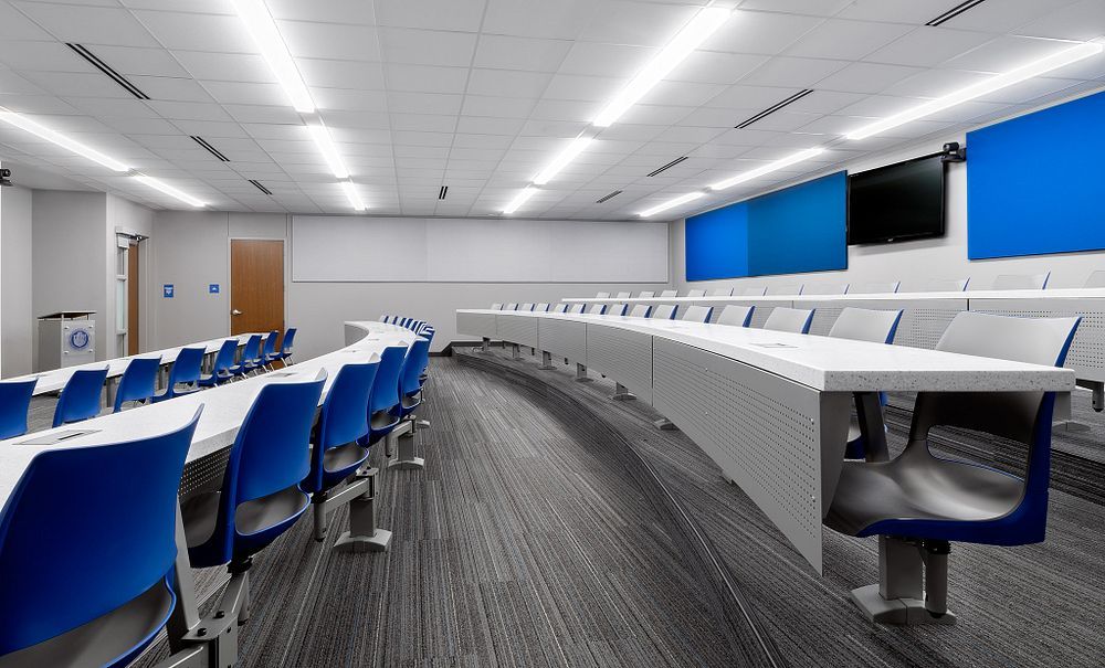 Empty modern lecture hall with blue chairs, curved white desks, and large wall screens