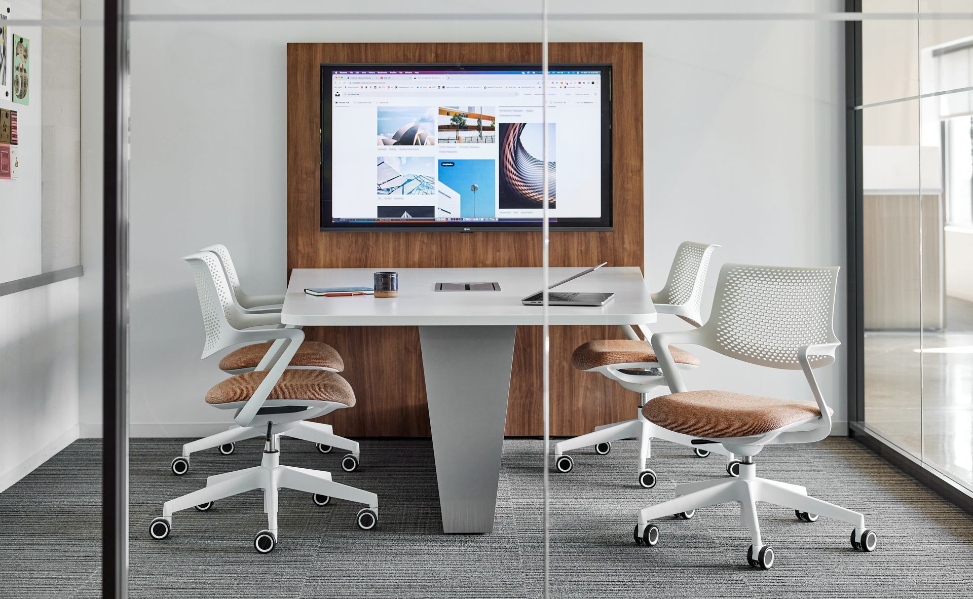 Modern office conference room with glass walls, a large screen, and white chairs around a central table