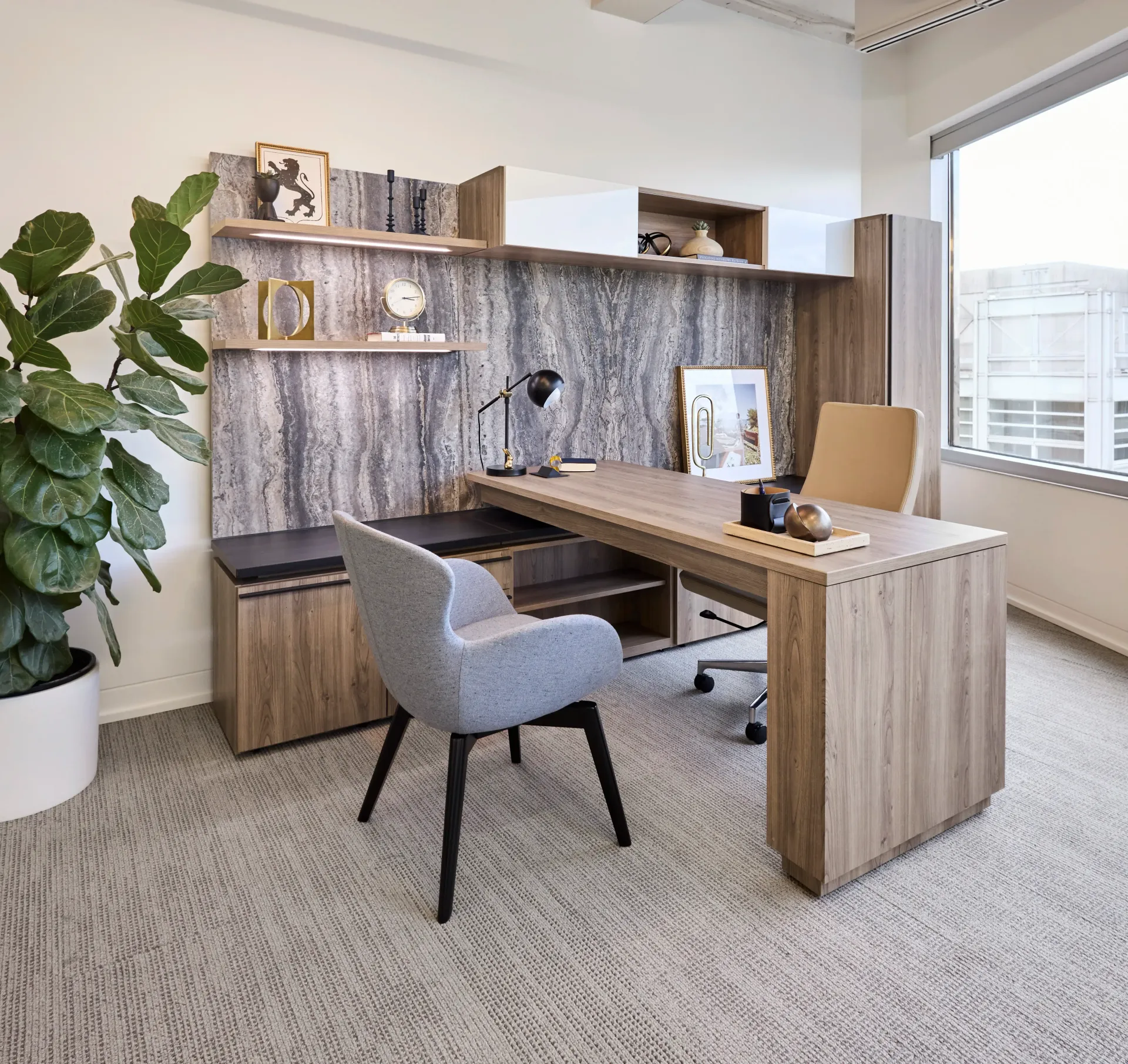 Modern home office with wood desk, gray chair, shelving, and a large plant by the window