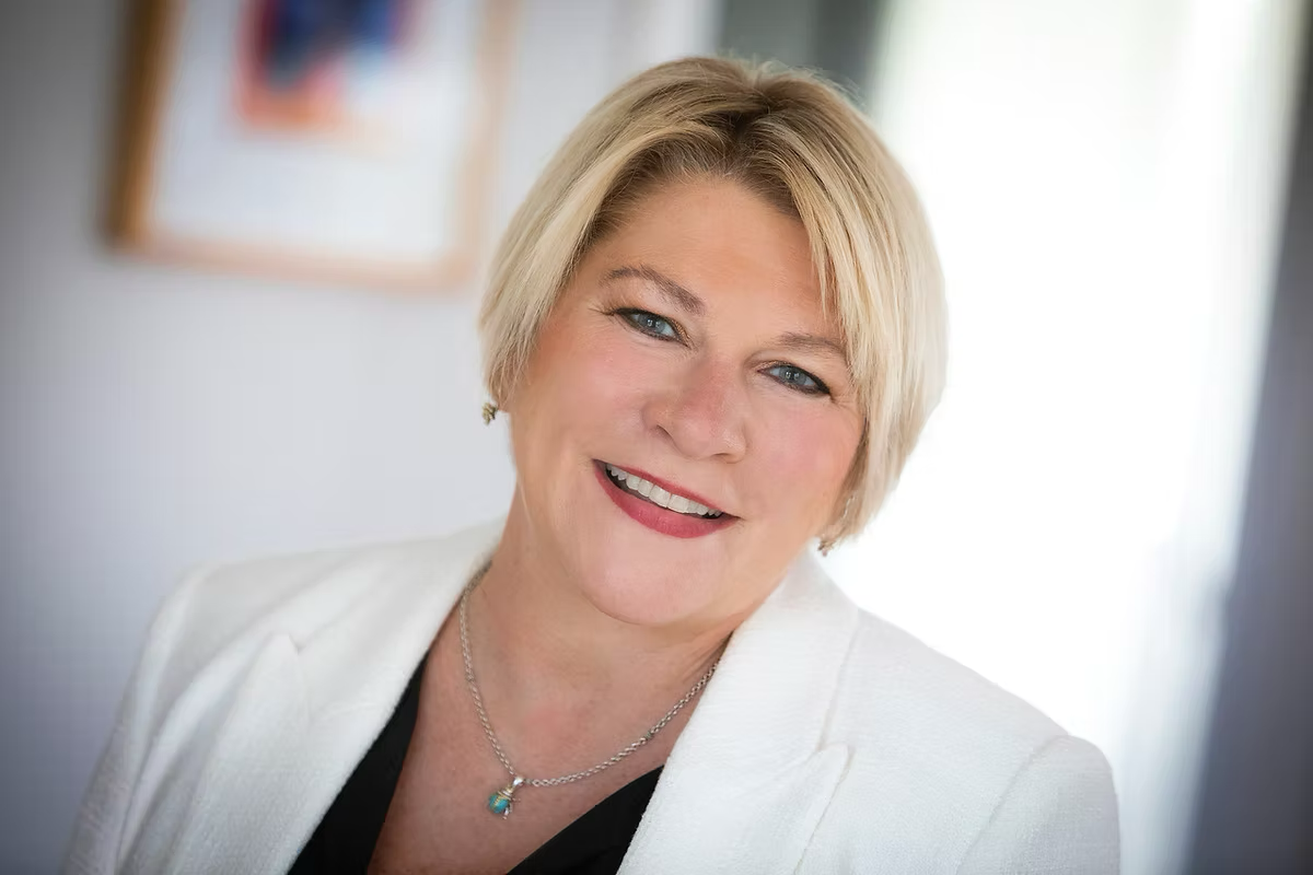 A woman in a white jacket and black shirt is smiling for the camera.
