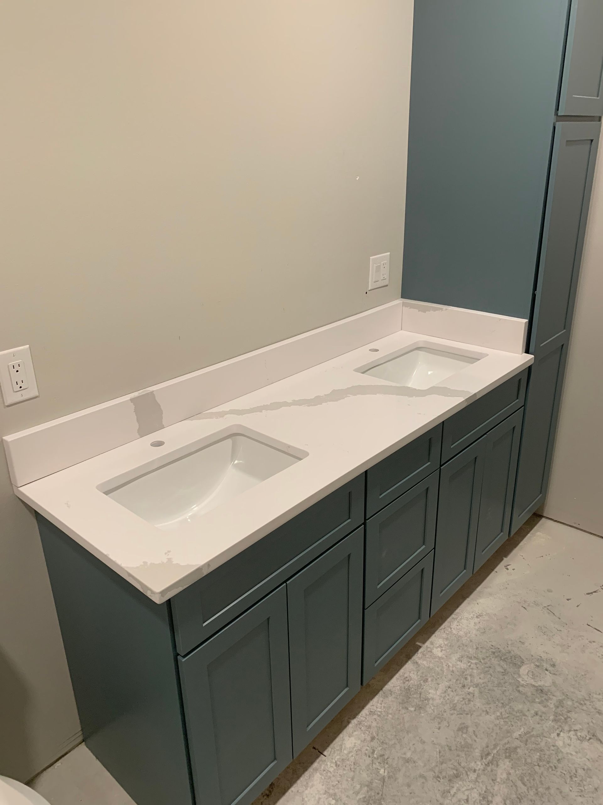 Blue bathroom vanity with two sinks and white countertop against a light gray wall.