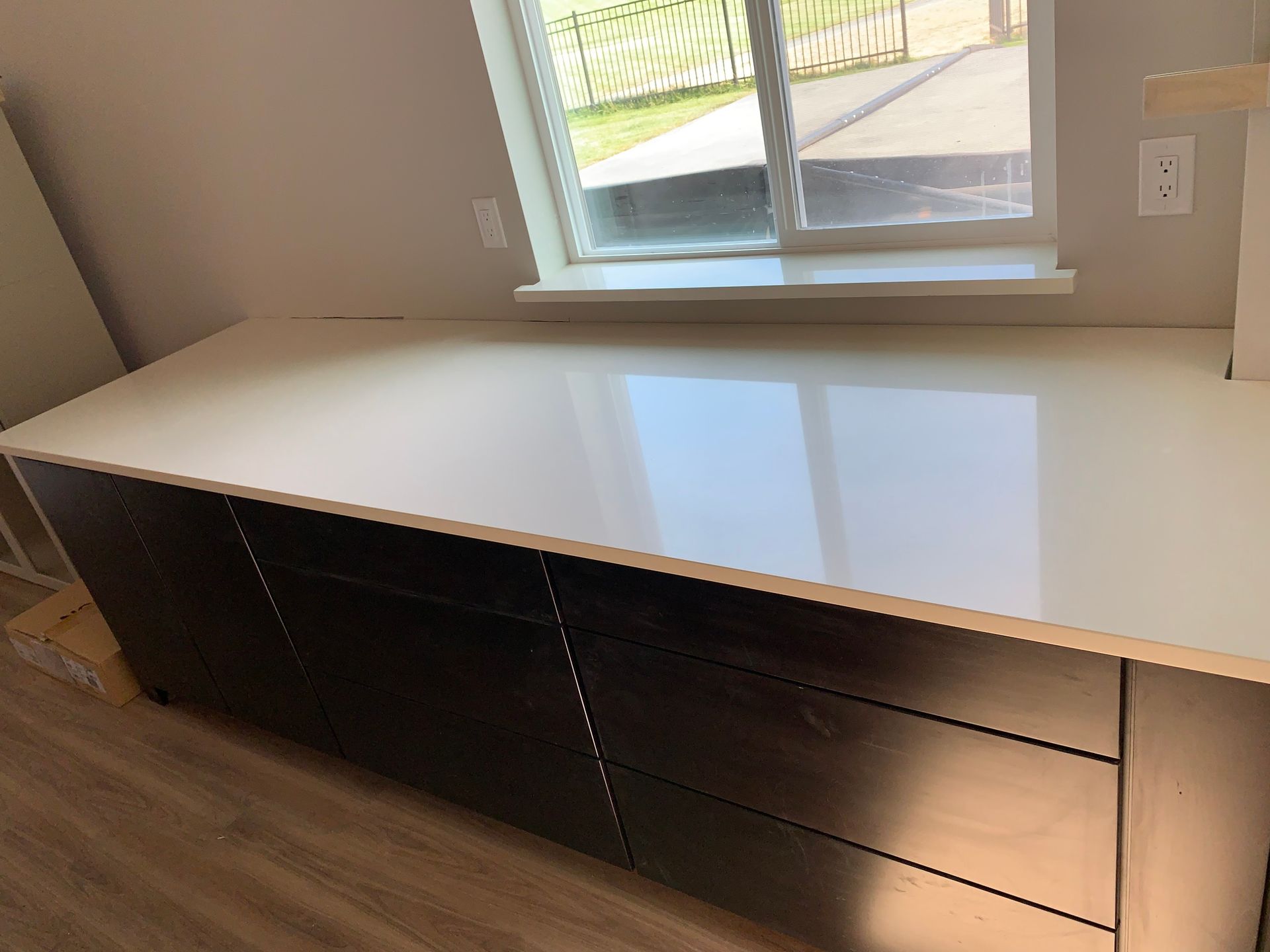 White countertop over dark wood cabinets, next to a window.
