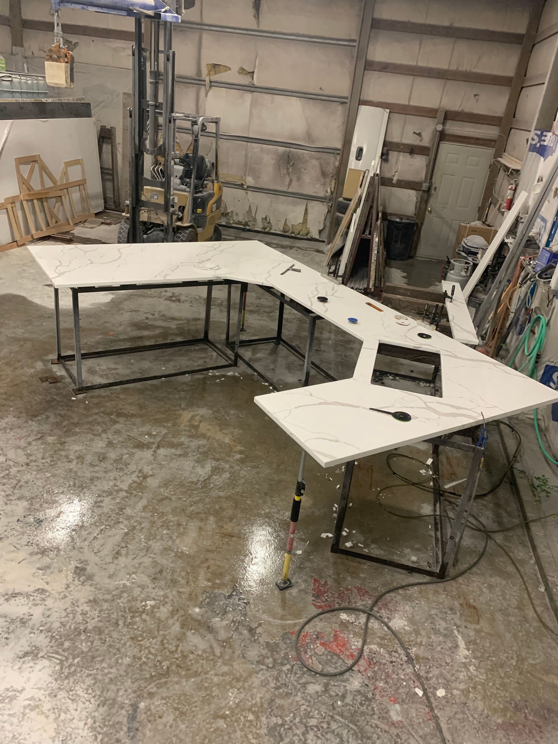 L-shaped desk with white marble top on black metal legs in a workshop setting.