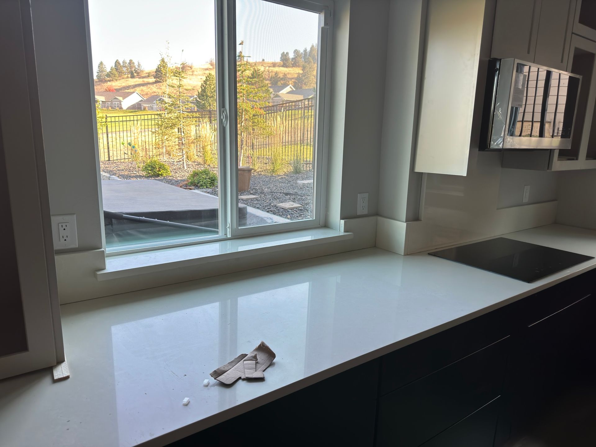 Kitchen countertop with a window overlooking a yard. White quartz surface, dark cabinets, and a modern stovetop.