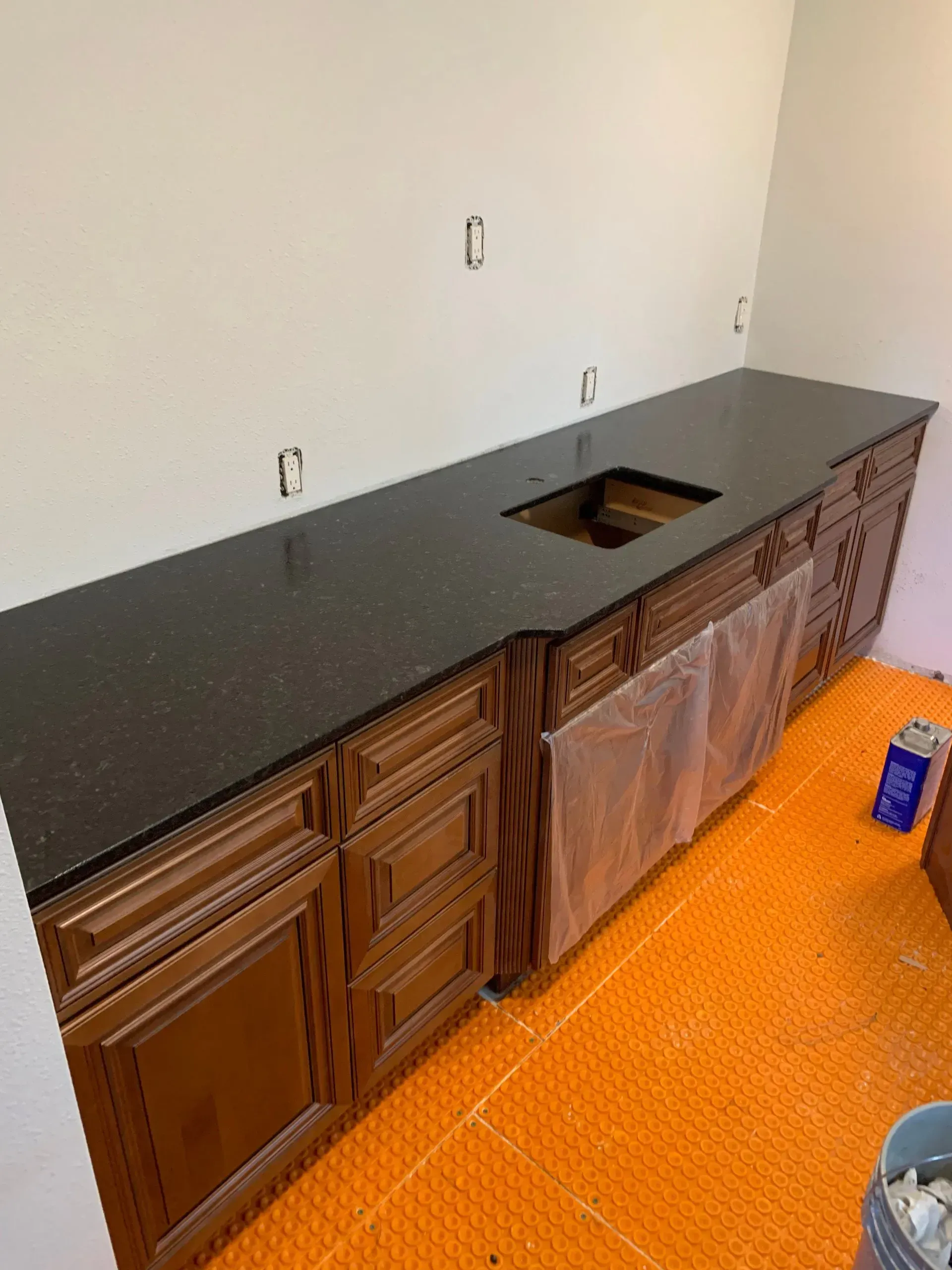 Dark countertop on brown cabinets with a sink cutout, orange floor, and unfinished wall.