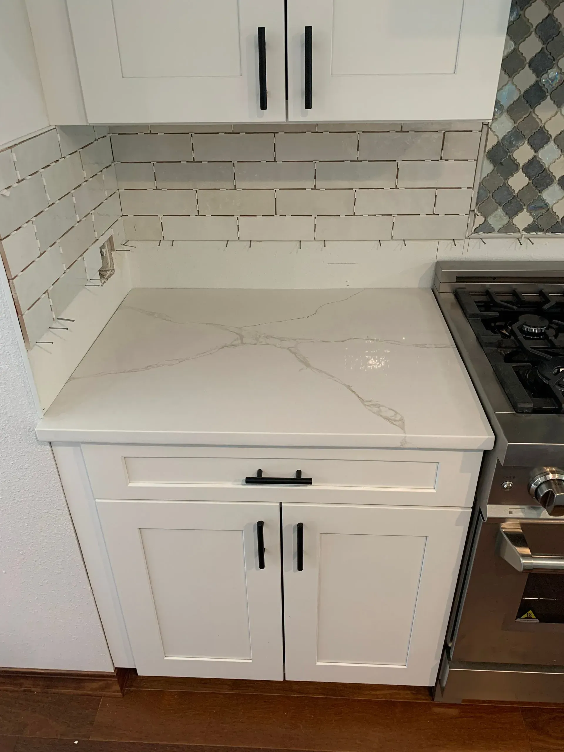 White kitchen cabinets with a white countertop, a gas range, and white and gray tile backsplash.