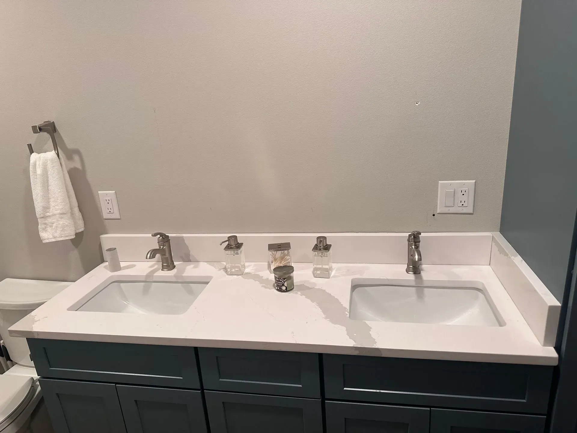 Bathroom with dual sinks, white countertops, dark blue cabinets, gray walls, towel holder.