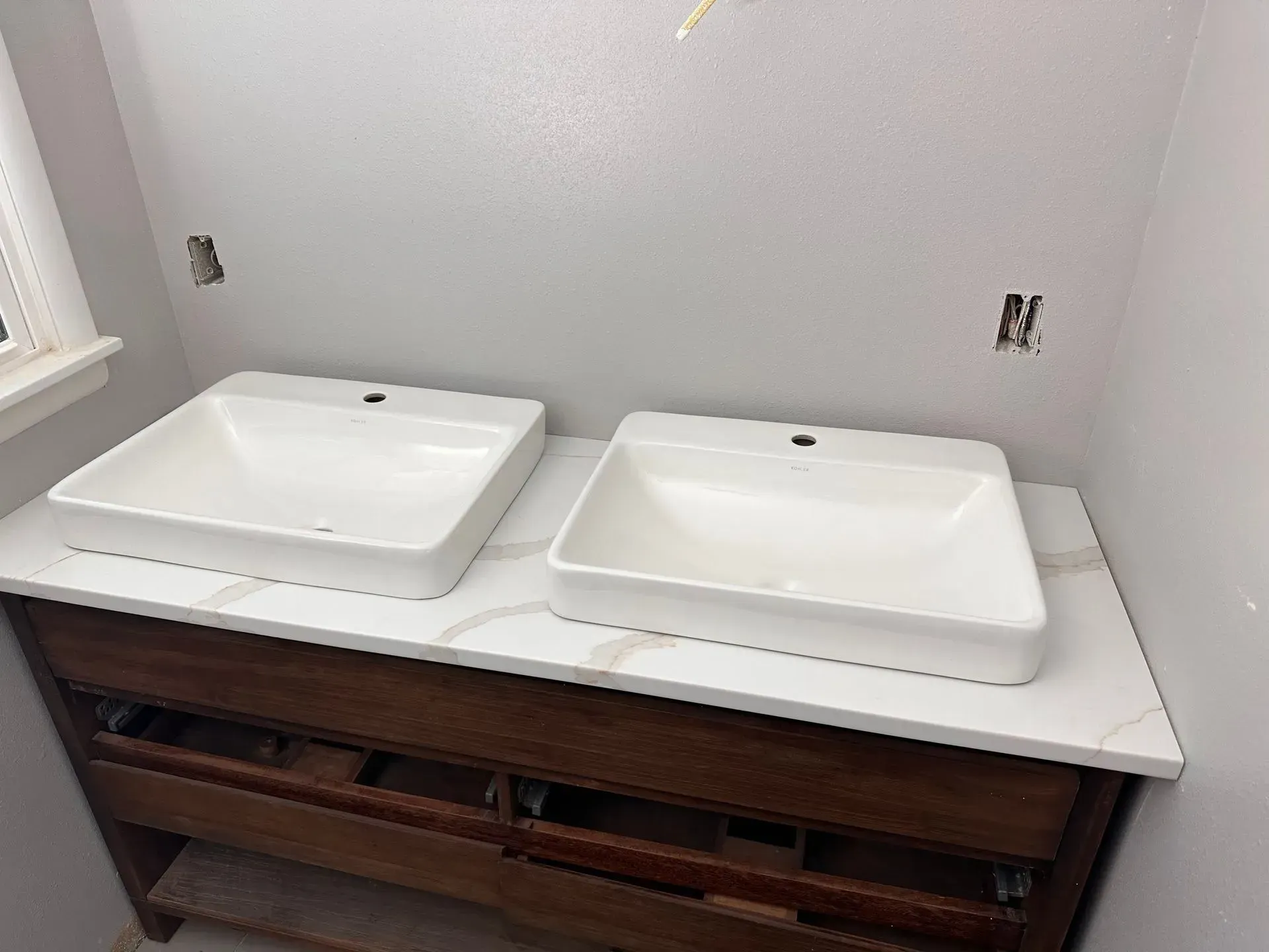 Bathroom vanity with two white square sinks on a marble countertop; dark wood cabinet.