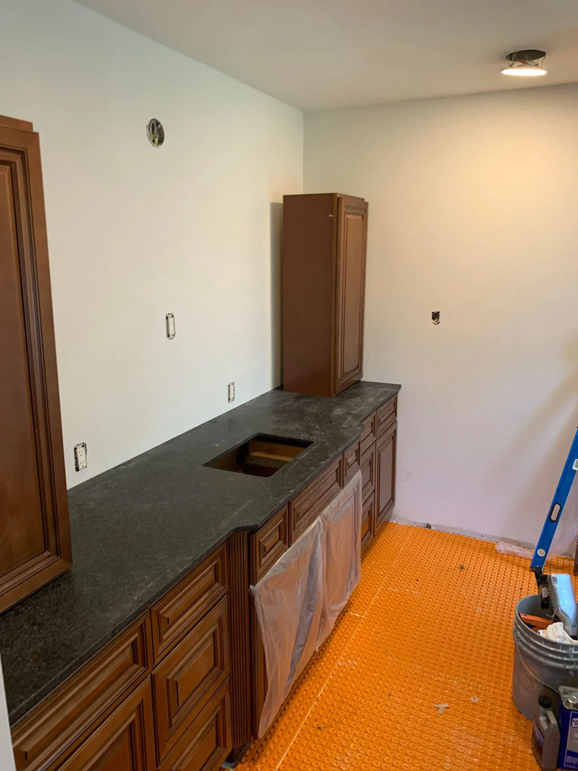 Kitchen renovation in progress: dark cabinets, black countertop, orange floor heating, white walls.