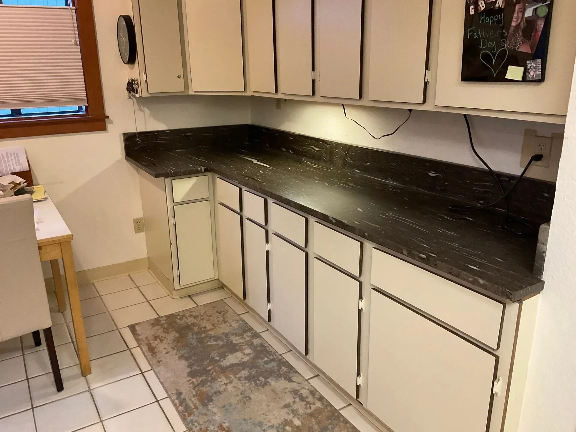 Kitchen with white cabinets, dark countertop, and a rug.