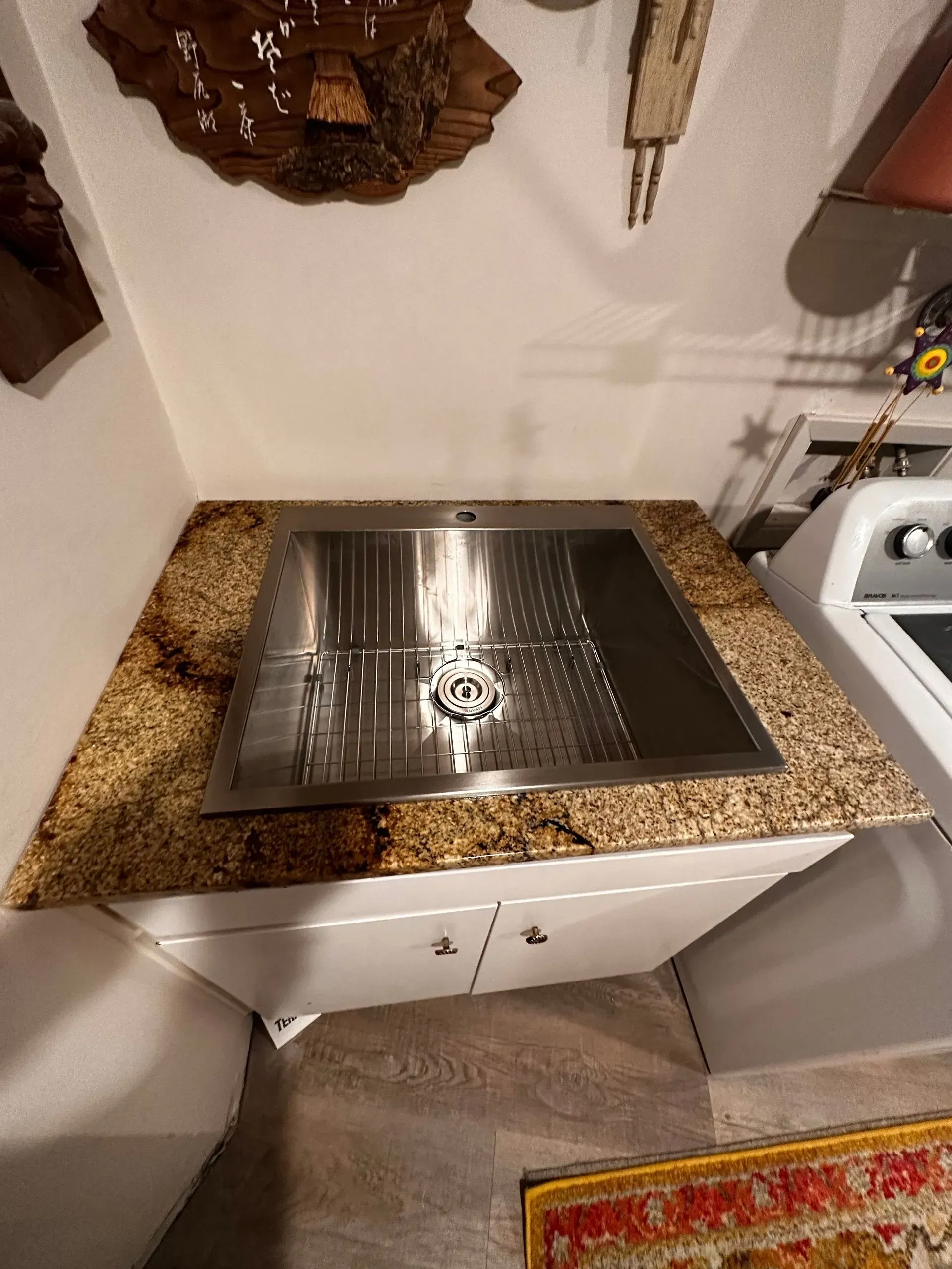 Stainless steel sink in a granite countertop on a white cabinet, near a washing machine.
