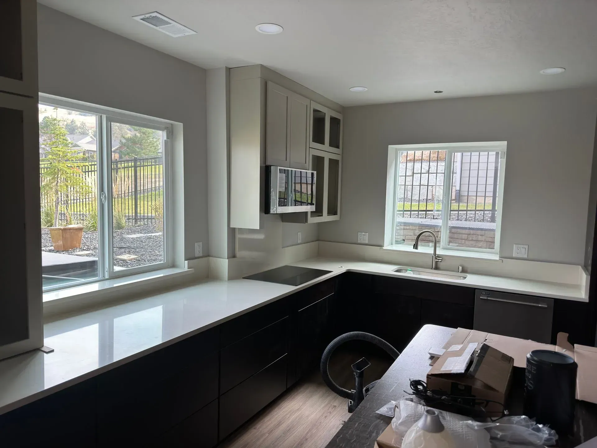 Modern kitchen with dark cabinets, white countertops, and two windows.