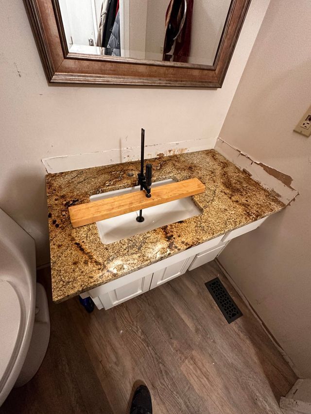 Bathroom vanity with granite countertop, white cabinet, sink, and faucet, damaged wall.