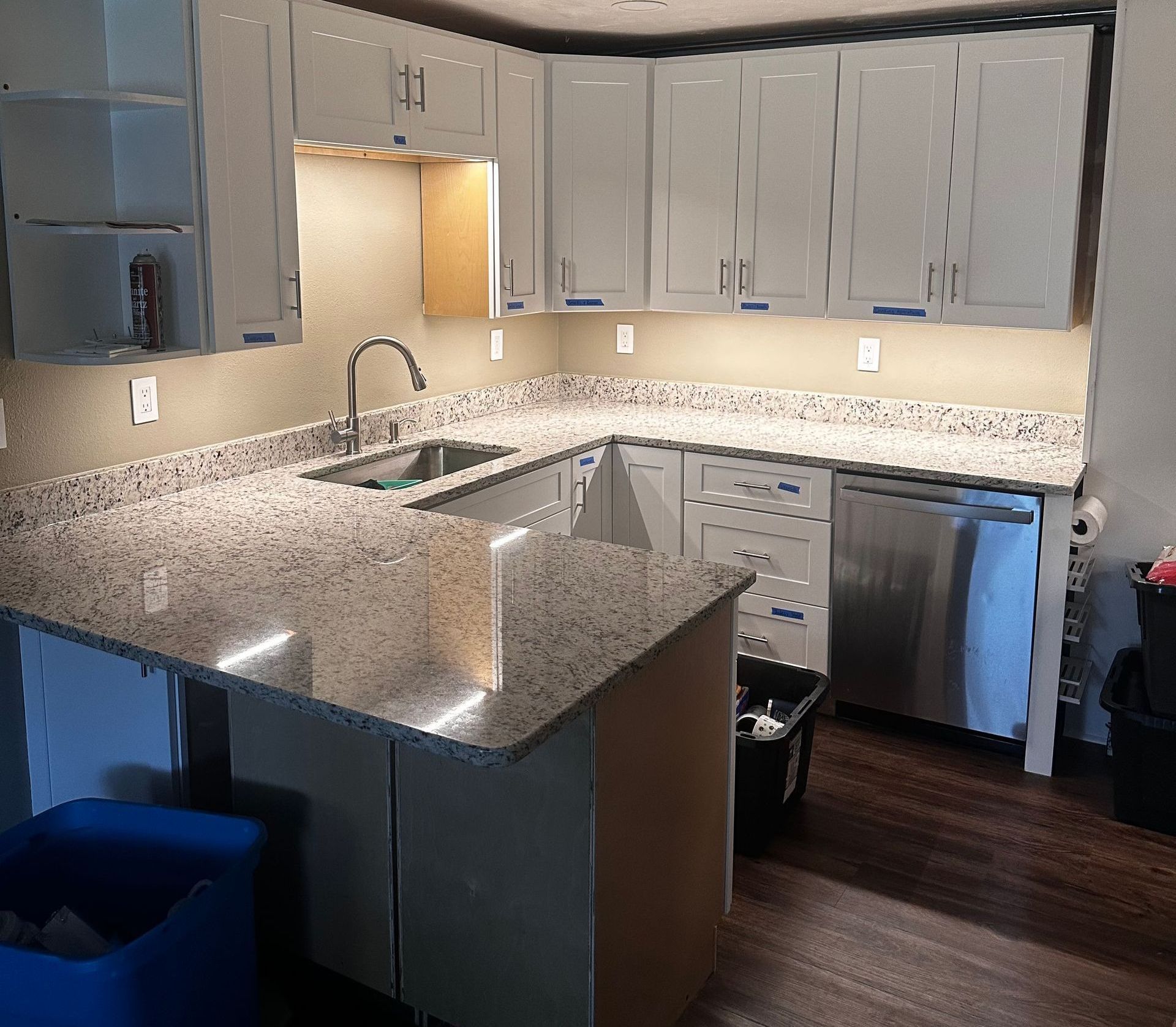 Kitchen remodel in progress: white cabinets, granite countertops, stainless steel appliances, and dark flooring.