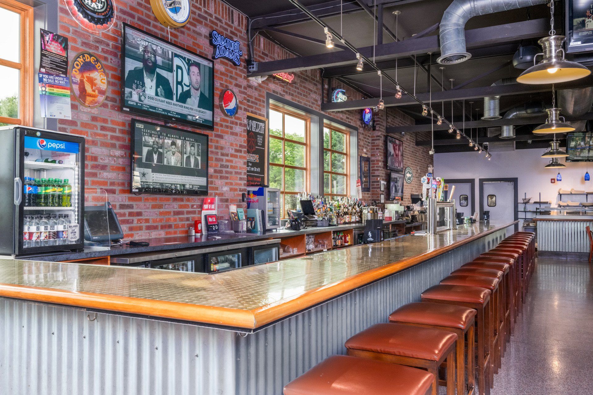 A long bar with stools and a refrigerator in a restaurant.