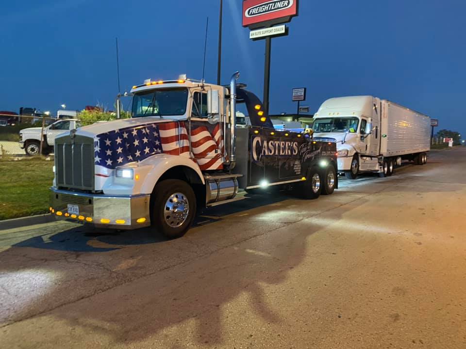 A tow truck with an american flag on it is parked on the side of the road.