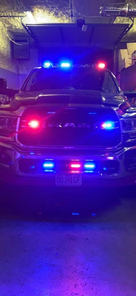 A dark-colored Ram truck with flashing red and blue emergency lights in a garage setting.