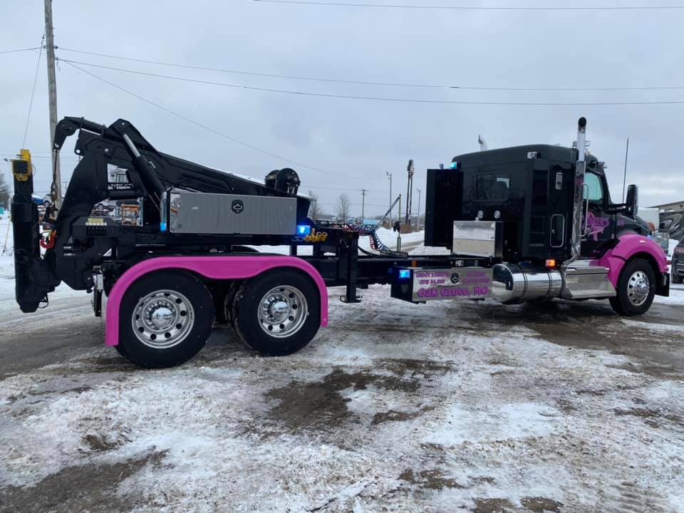 A pink and black tow truck on a snowy street. The truck has pink accents and a large towing apparatus.