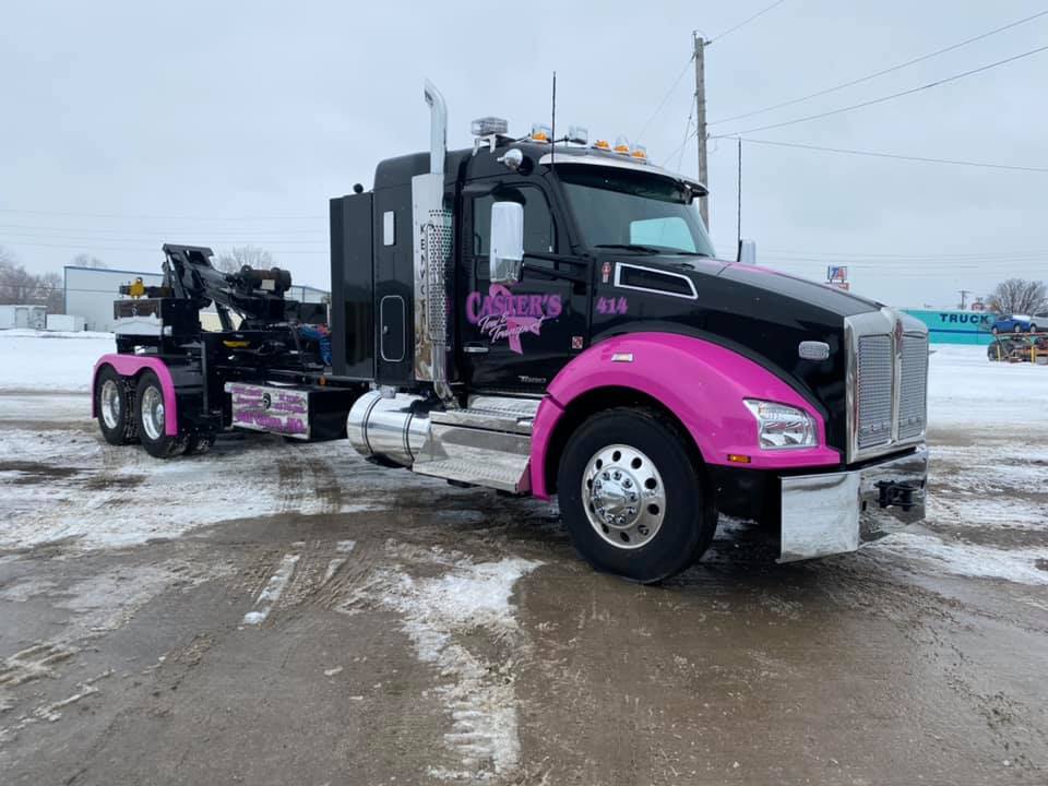 Black semi-truck with pink accents, parked on snow-covered pavement. Front fenders and details are pink.