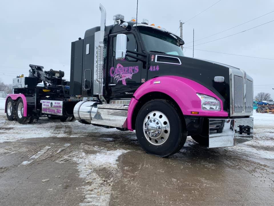 Black and pink semi-truck parked on a snowy, icy surface.