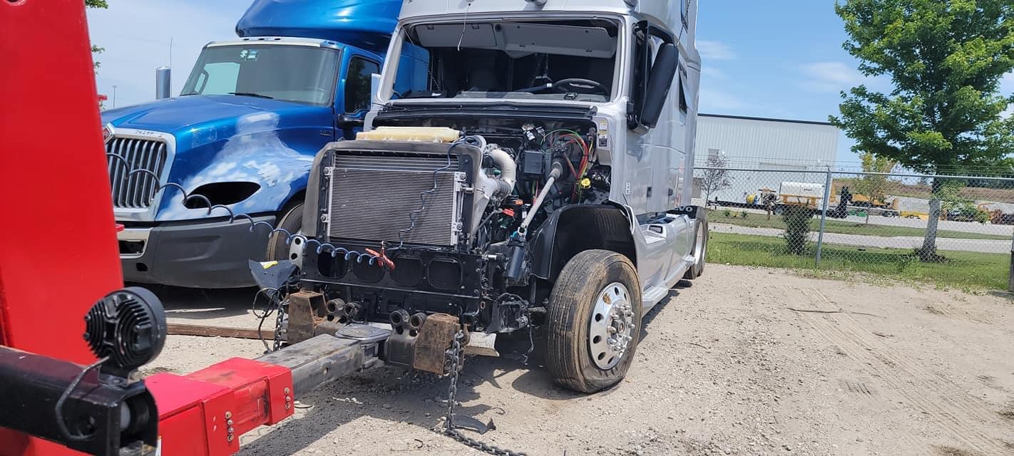 A partially dismantled silver semi-truck parked outside, with a blue truck in the background.