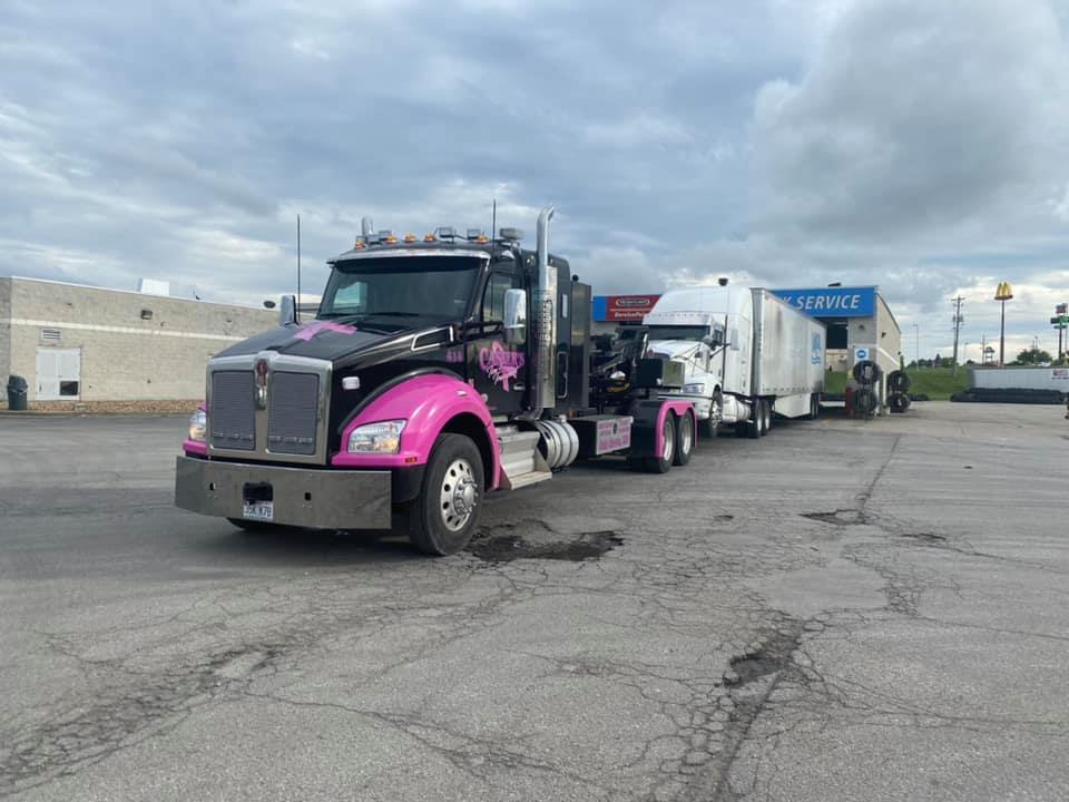 Black and pink semi-truck towing two trailers in a parking lot on a cloudy day.
