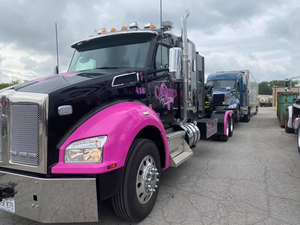 Black and pink semi-truck parked outside, with a second blue truck and trailer behind it.