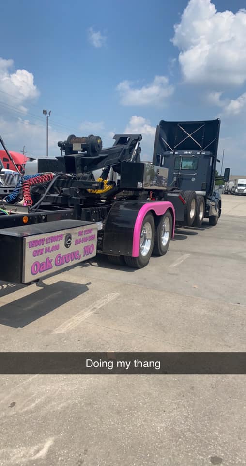 Tow truck with pink fenders; parked outside on a sunny day. Text: 