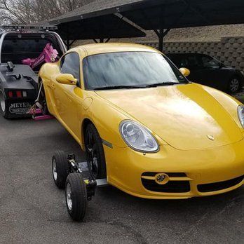 Yellow Porsche sports car being towed. The front wheels are on a dolly. A tow truck is visible in the background.