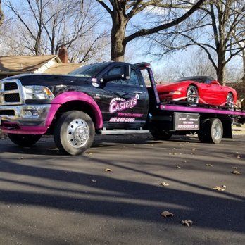 Black and pink tow truck with a red sports car on the flatbed, parked on a street.