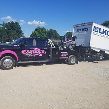 A black tow truck with pink accents hauling a large white trailer with 