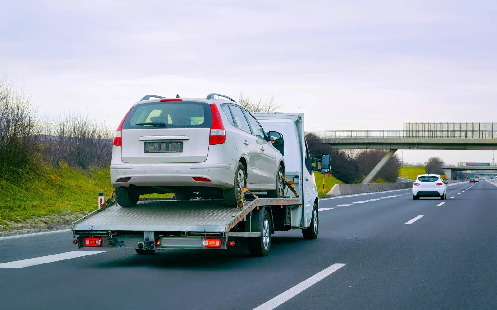A tow truck is towing a white car on a highway.
