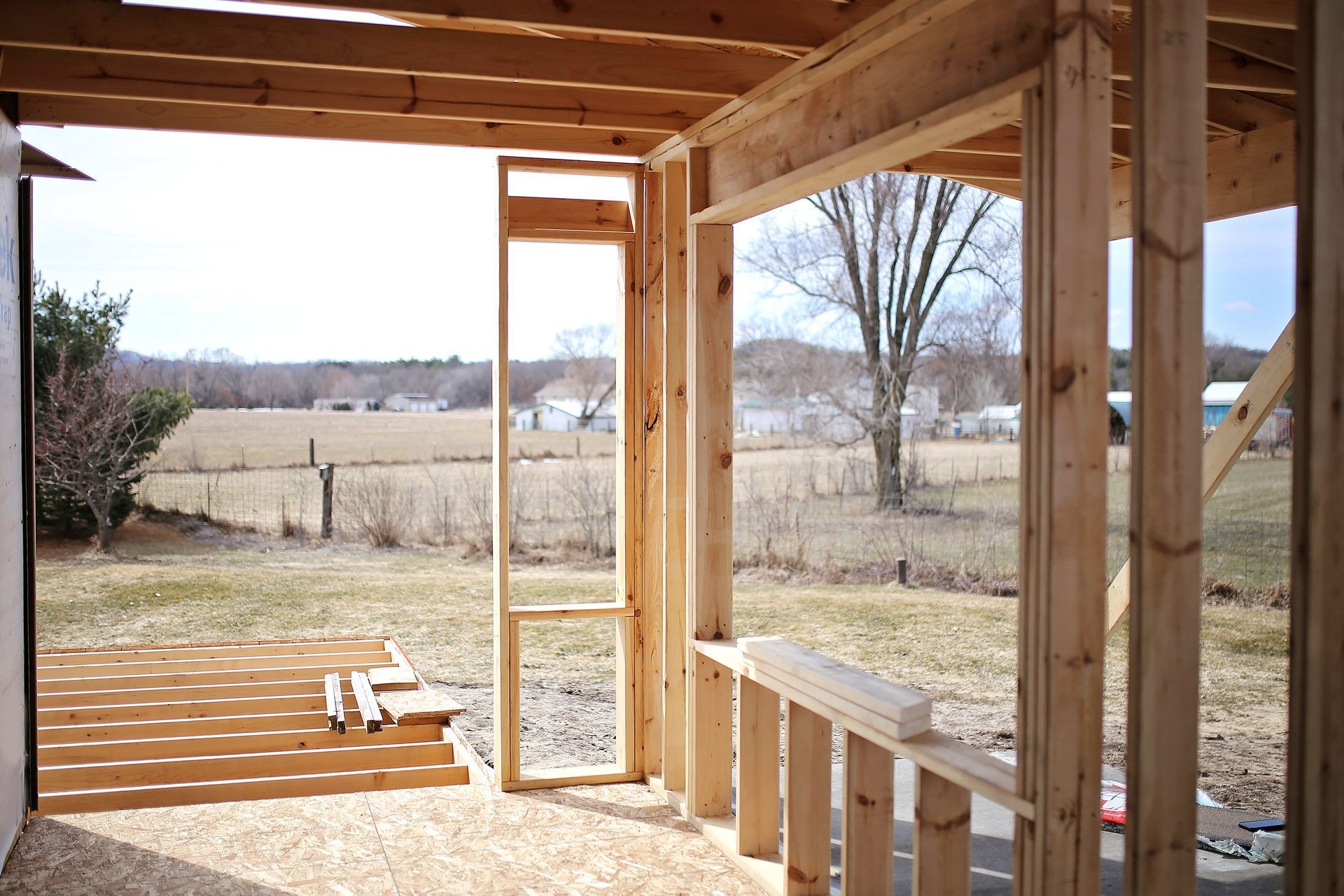 Framing of an outdoor porch under construction with a rural landscape visible.