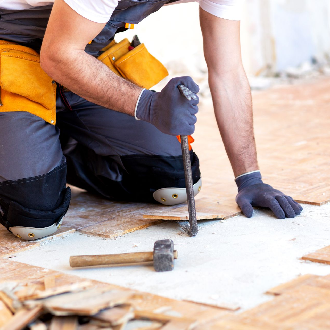 Person removing floorboards with a hammer and chisel. Kneeling, wearing gloves and tool belt. Person removing floorboards with a hammer and chisel. Kneeling, wearing gloves and tool belt.