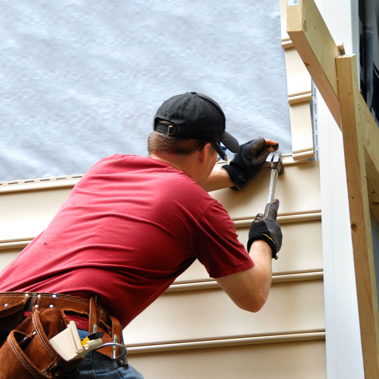 Construction worker hammers siding onto a house wall outdoors.