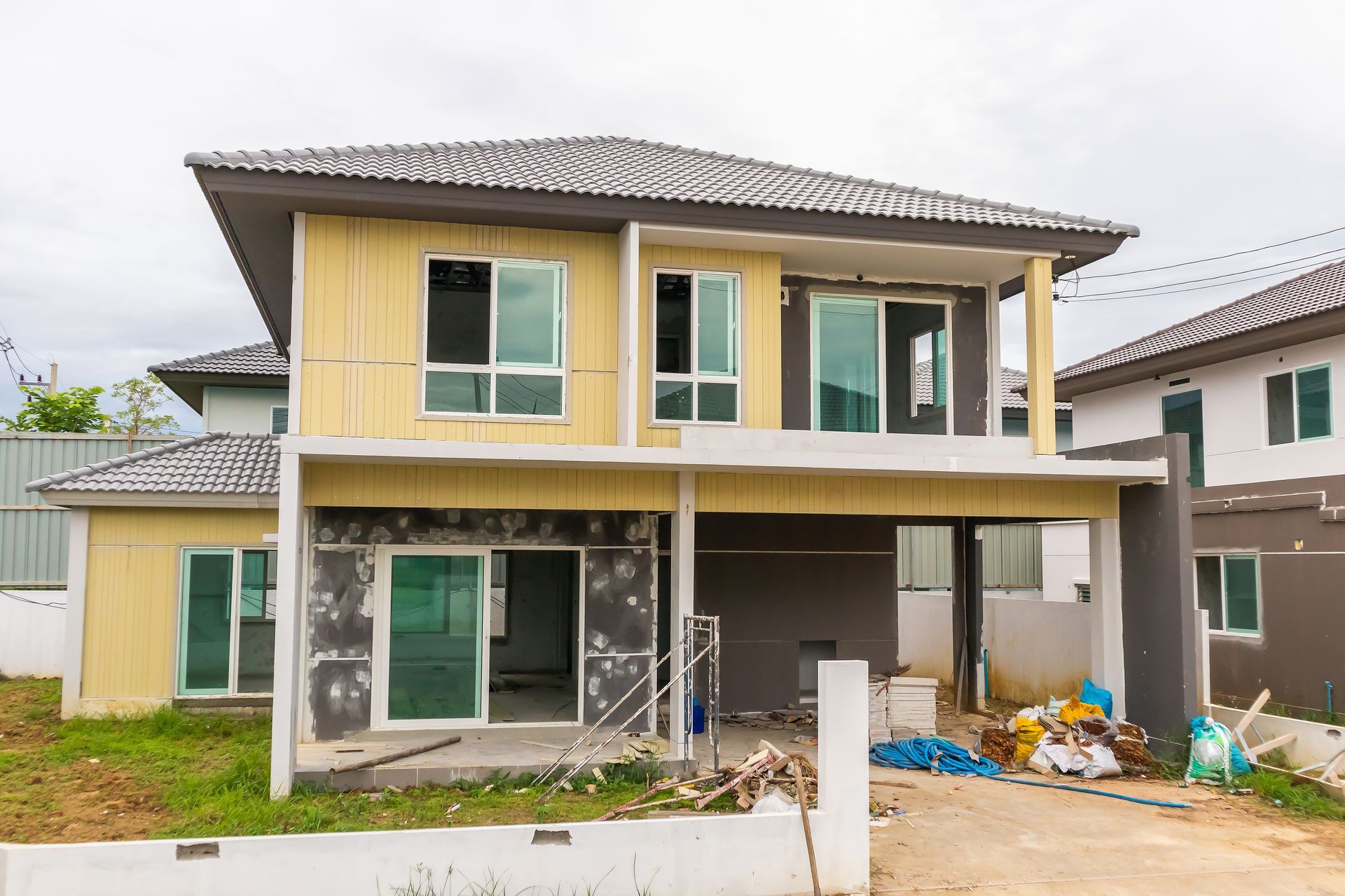 Two-story house under construction, yellow and gray siding, white window frames, cloudy sky.