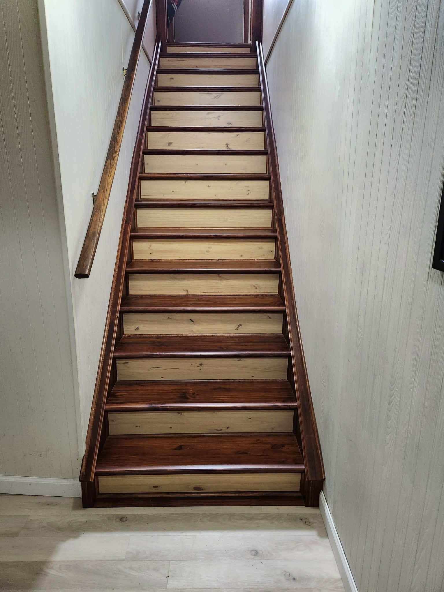 Interior of a narrow, industrial kitchen with stainless steel counters, cabinets, and ventilation pipes.