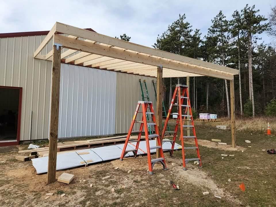 Person on a ladder painting the trim of a two-story gray house. Three other ladders are placed against the house.