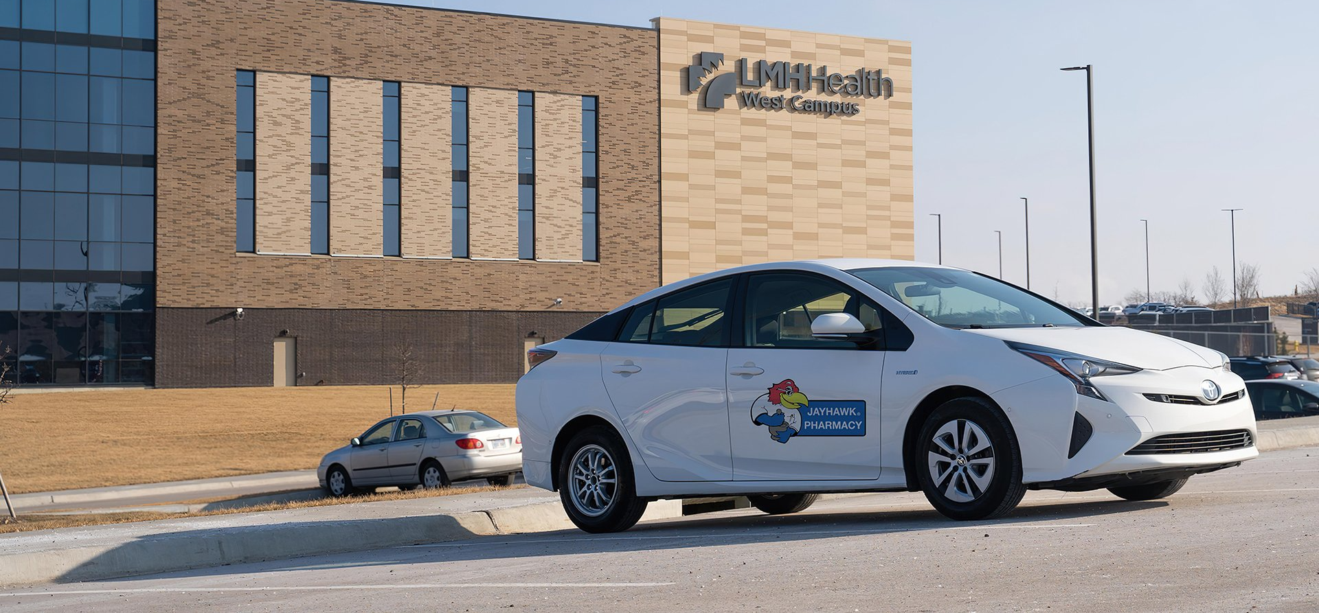 A white car is parked in front of a large building.