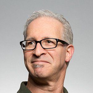 Portrait of a man with gray hair and black glasses looking off to the side against a gray background