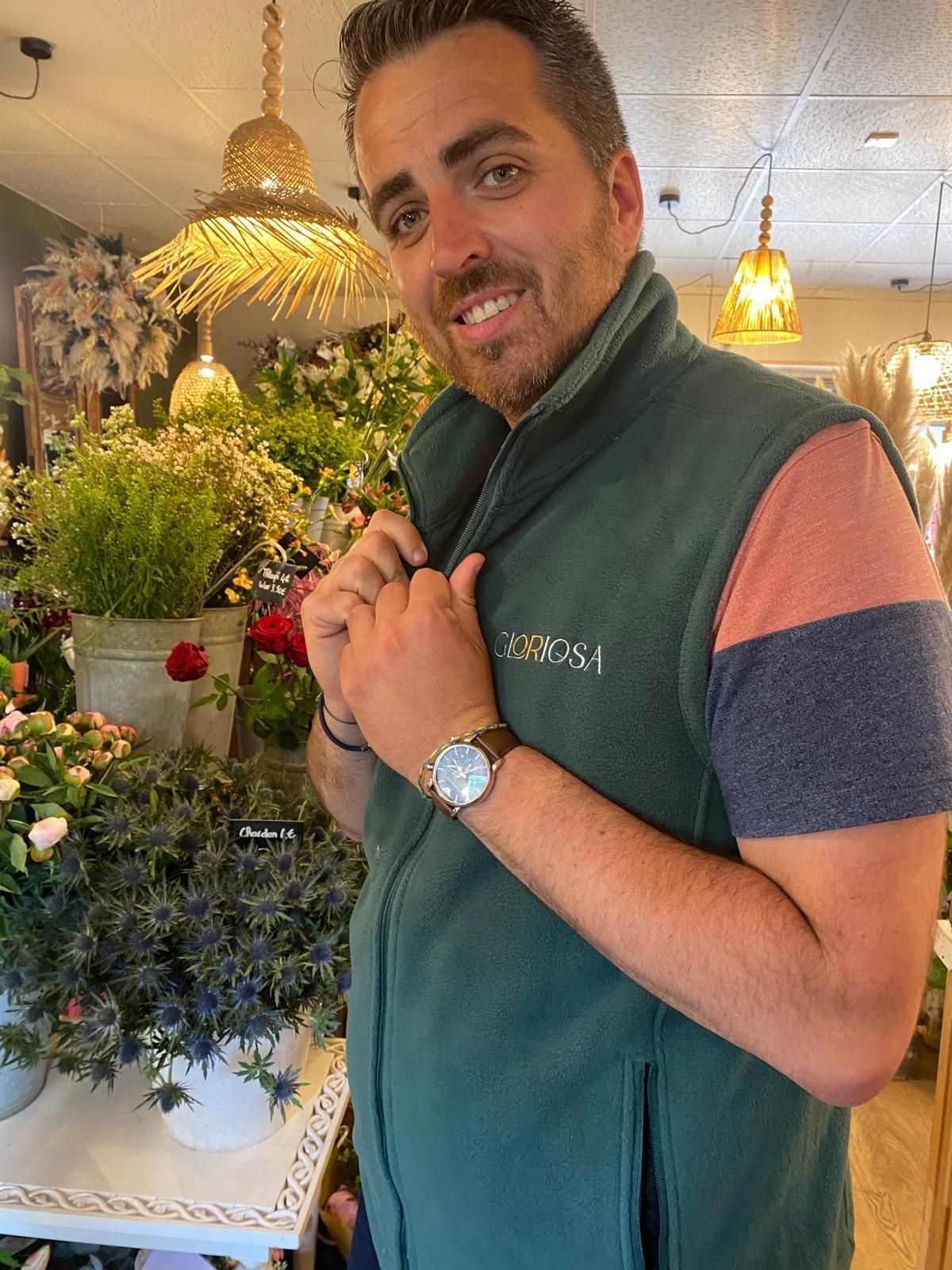 Un homme portant une polaire sans manche devant un présentoir rempli de fleurs.