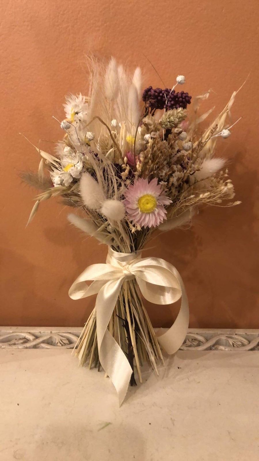 Un bouquet de fleurs séchées avec un nœud blanc est posé sur une table.