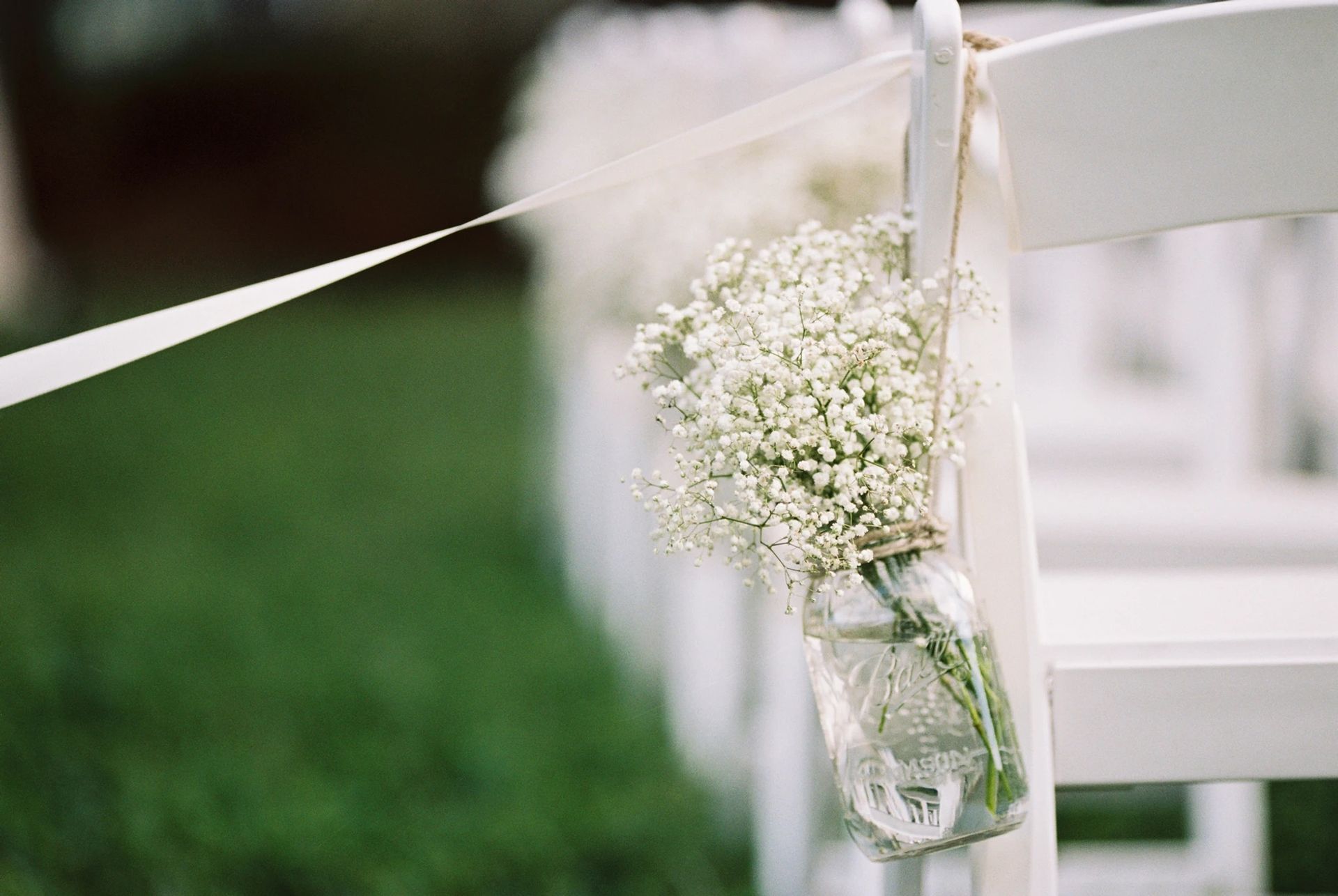 Une rangée de chaises blanches avec des bocaux Mason remplis de gypsophile suspendus.