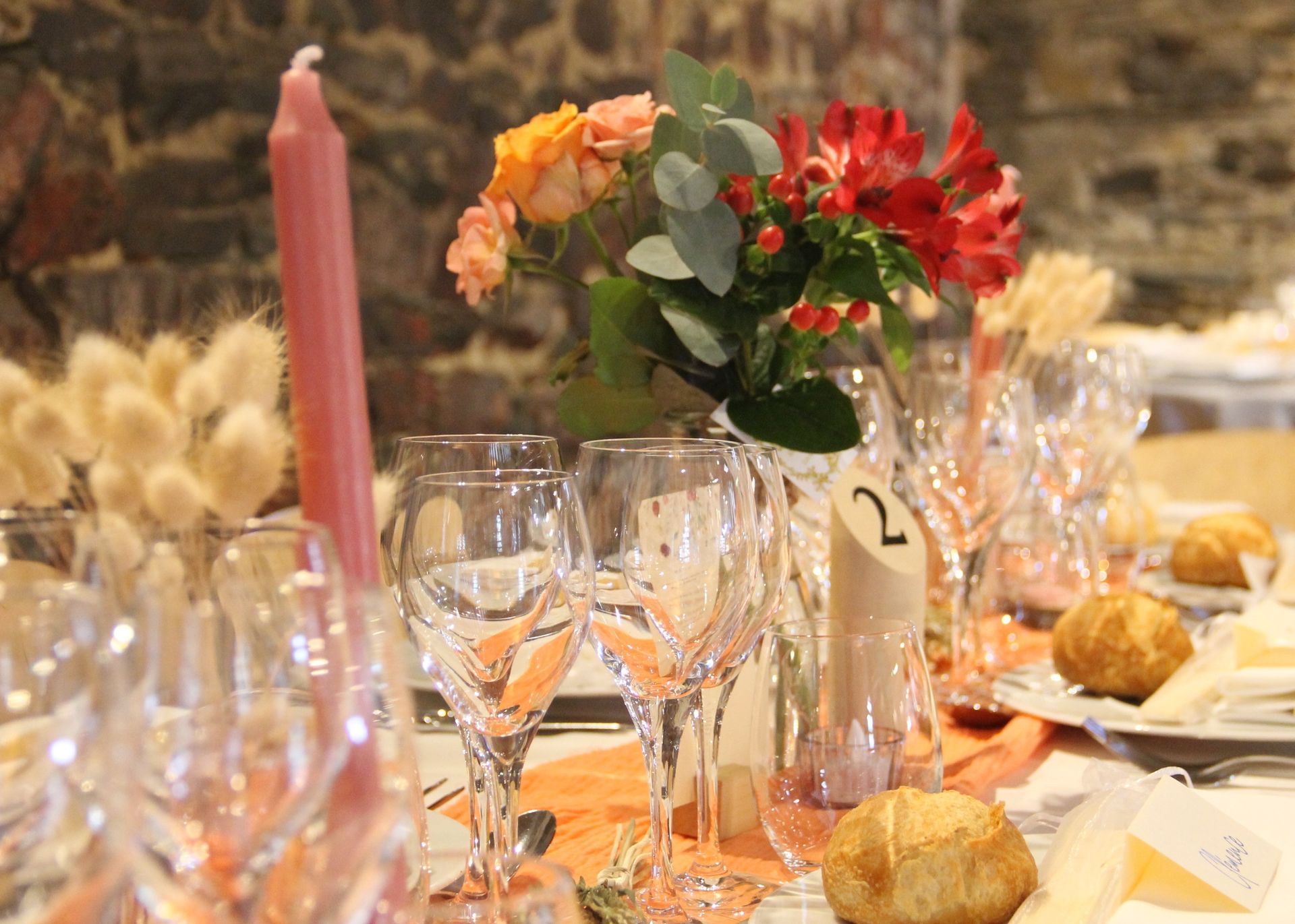 Une table dressée pour une réception de mariage avec des verres à vin, des bougies et des fleurs.