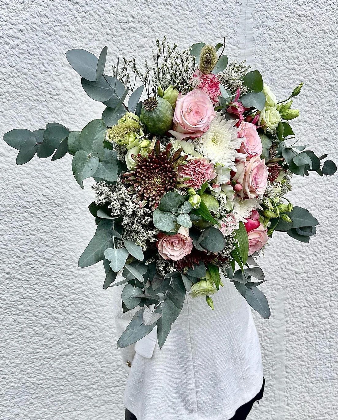 Une personne tient un bouquet de fleurs devant un mur blanc.