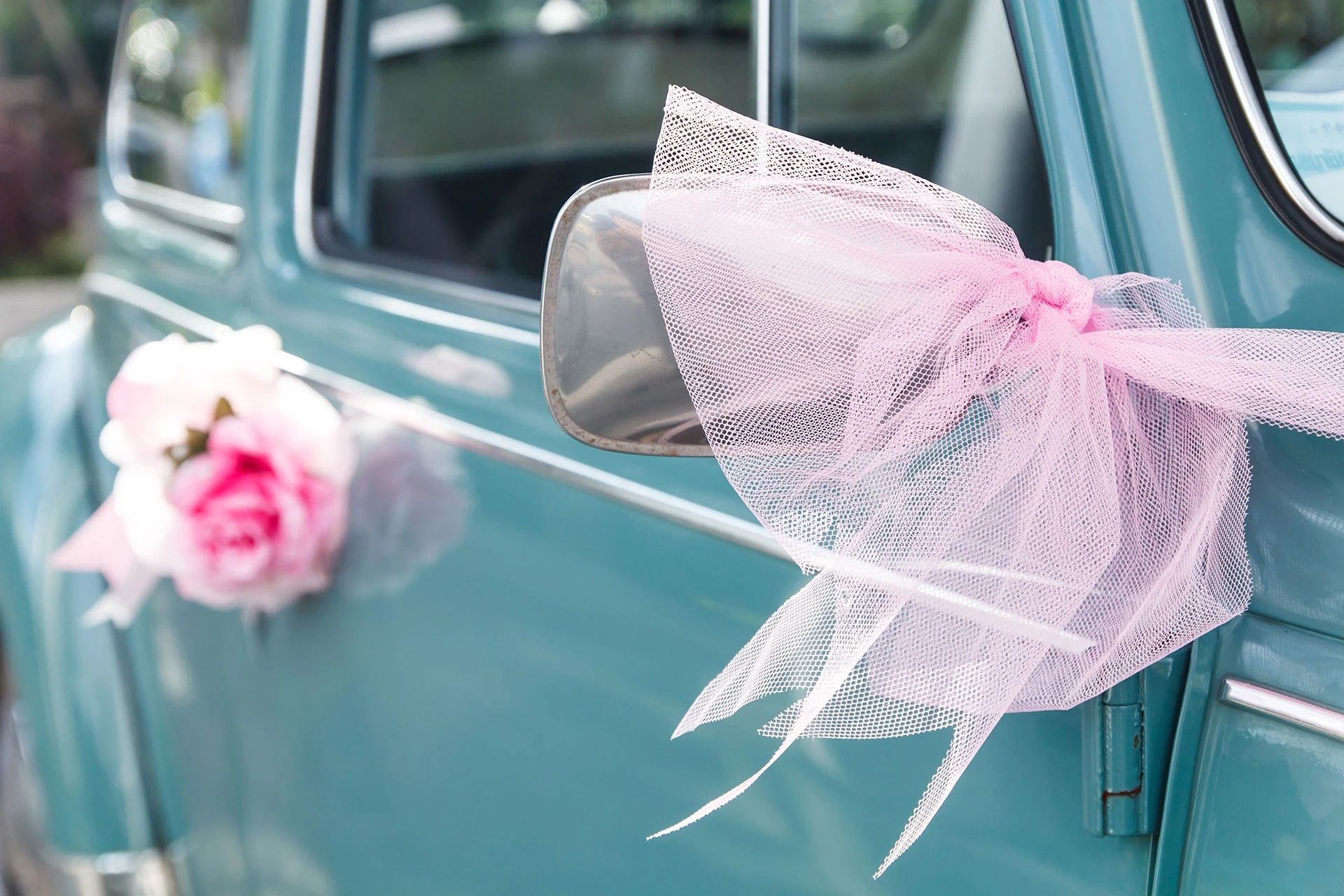 Une voiture bleue décorée de nœuds et de fleurs roses.
