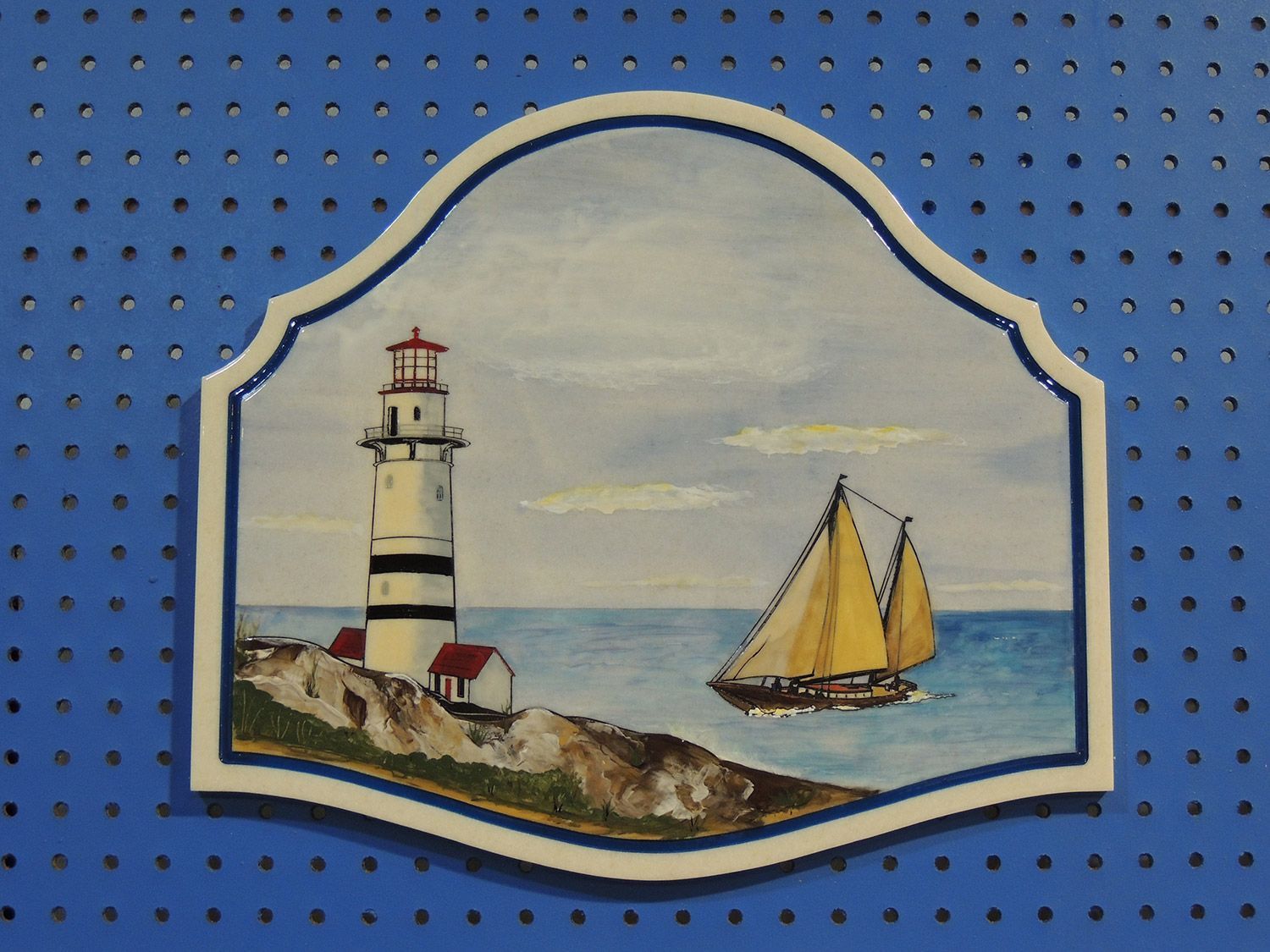Lighthouse and sailboat scene painted on a white-framed plaque with blue background.